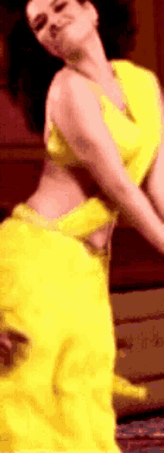a woman in a yellow saree is dancing in a room .
