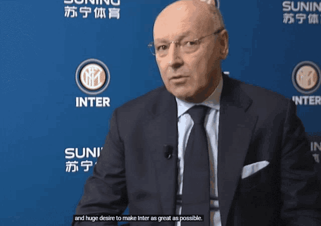 a man in a suit and tie is sitting in front of a blue background that says inter