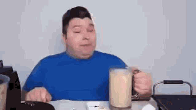 a man in a blue shirt is sitting at a table holding a glass of milk .