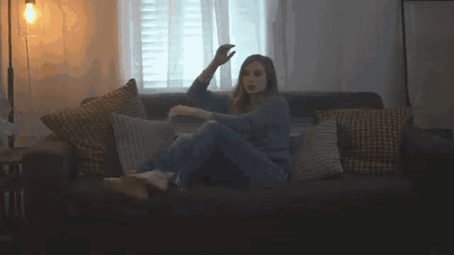 a woman is sitting on a couch in a living room with her feet up and making a funny face .
