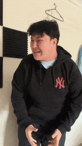 a man wearing a black ny yankees hoodie makes a funny face