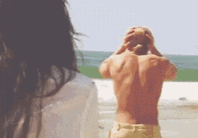 a man without a shirt is standing on a beach looking at the ocean