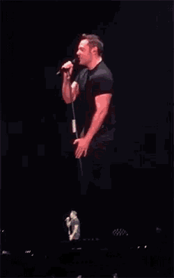 a man is standing on a stage singing into a microphone .