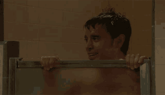 a man is taking a shower and smiling while peeking through the glass door .