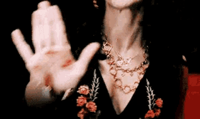 a woman in a black dress and gold necklace is making a stop sign with her hands .