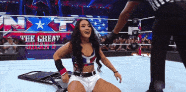 a woman is sitting on the ground in a wrestling ring while a referee stands behind her .