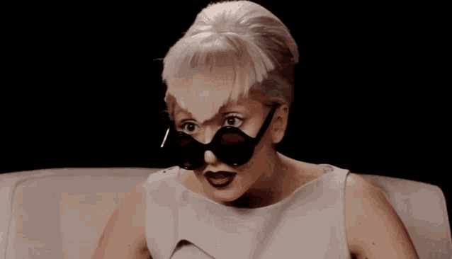a woman wearing a wig and sunglasses looks at the camera