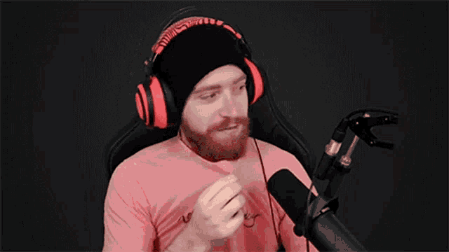 a man wearing headphones and a beanie is sitting in front of a microphone and covering his nose .