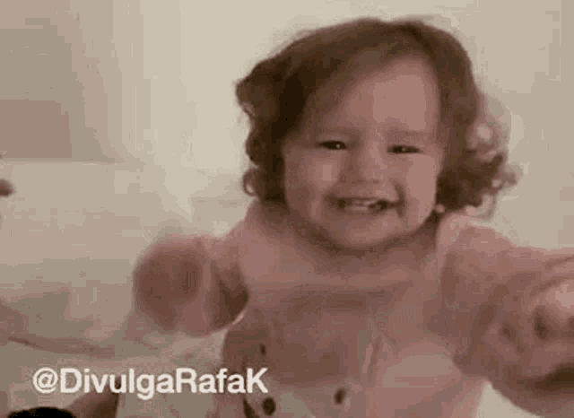 a baby girl is sitting on a bed and smiling at the camera .