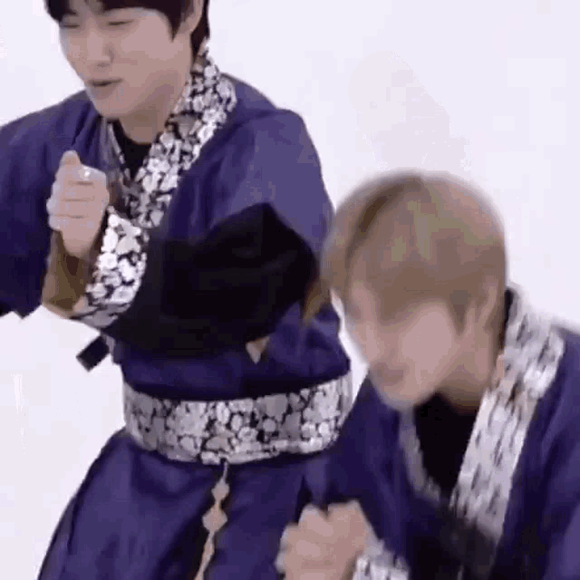 two men are standing next to each other in purple kimonos .