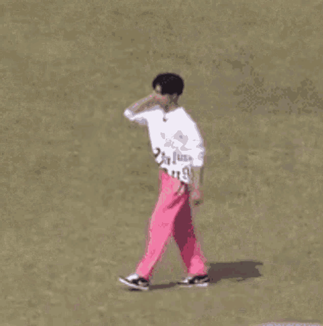 a man wearing a white shirt and pink pants is walking on a field .