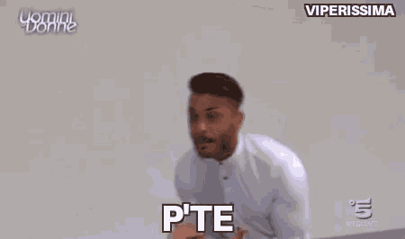 a man in a white shirt is standing in front of a wall and yelling at someone .
