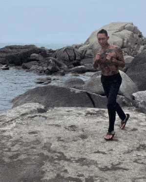 a man without a shirt is walking on a rocky beach near the ocean