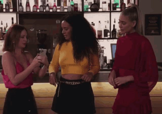 three women are standing in front of a bar and one of them is looking at a cell phone