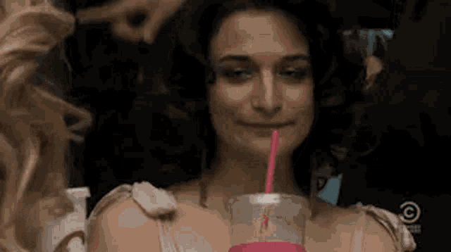 a woman is drinking a pink smoothie with a straw in her mouth .