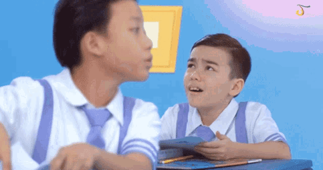 two young boys are sitting at desks in a classroom and one of them is holding a book