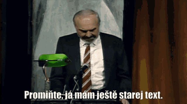 a man in a suit and tie stands in front of a green lamp with the words promine ja mam jeste starej text written below him