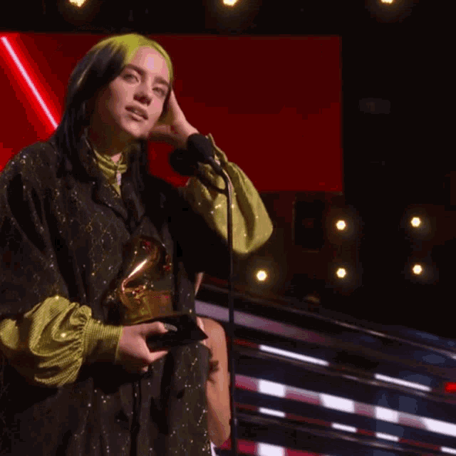 a woman with green hair holds a grammy trophy
