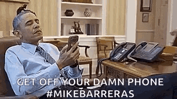 barack obama is sitting in a chair using a cell phone .