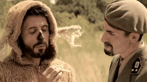 a man in a teddy bear costume is smoking a cigarette while another man in a beret looks on .