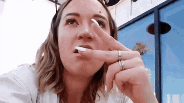 a woman with long white nails is eating a candy bar with her finger in her mouth .