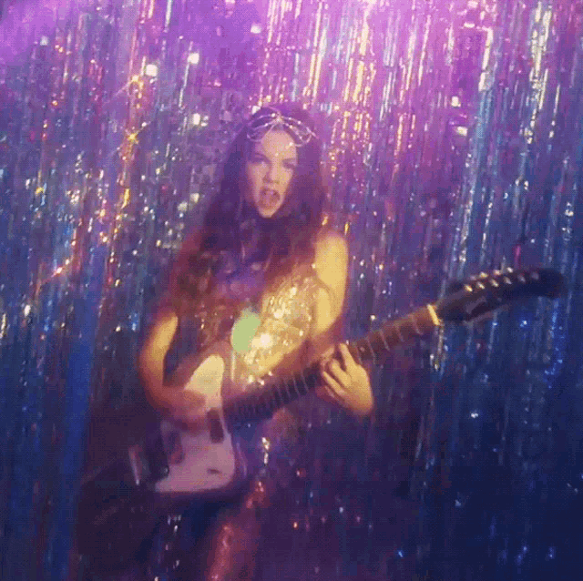 a woman in a sequined outfit is playing a guitar
