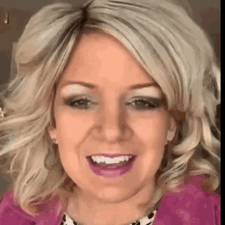 a woman with blonde hair and a pink jacket is smiling .