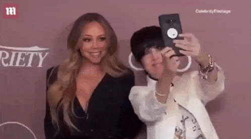 a woman is taking a selfie with mariah carey while standing next to her .