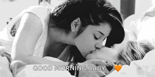 a black and white photo of two women kissing each other on a bed .