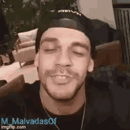 a man wearing a black hat and a black shirt is smiling and looking at the camera .