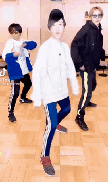 three people are dancing on a wooden floor in a room .