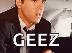 a man in a suit and tie is sitting in the back seat of a car with the word geez written on the screen .