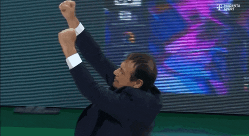 a man in a suit is raising his arms in the air in front of a magenta sport screen