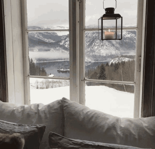 a window with a view of a snowy mountain and a candle hanging from it