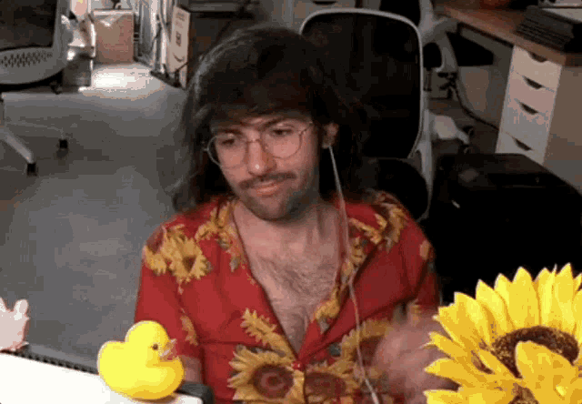 a man in a sunflower shirt is sitting at a desk with a rubber duck and a sunflower
