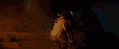a man in a black cape is standing next to a robot in a dark room .