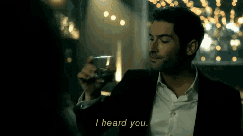 a man in a suit is holding a glass of whiskey and says i heard you