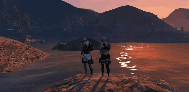 two people standing on a rock near a body of water with mountains in the background