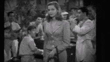 a woman in a suit is standing in front of a man playing a piano .