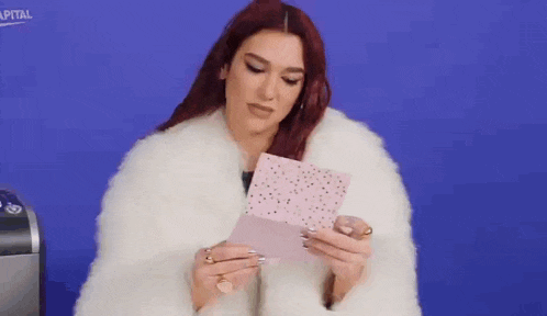 a woman in a white fur coat is holding a piece of paper in her hands .