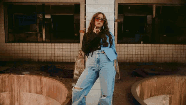 a woman wearing sunglasses and ripped jeans is standing in front of a building