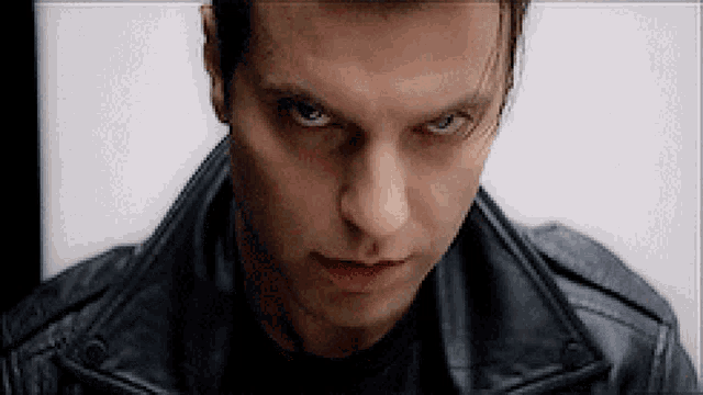 a man in a black leather jacket looks at the camera with a serious look on his face