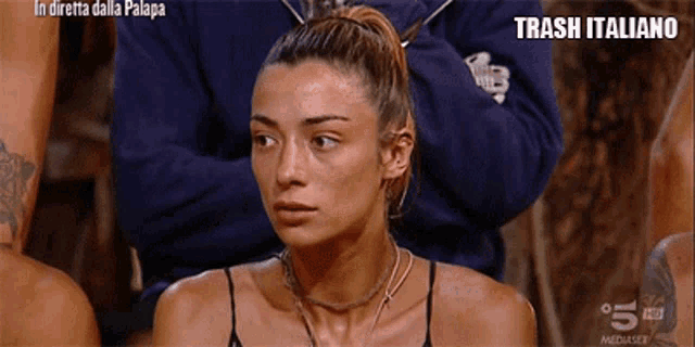 a woman in a black tank top is sitting in a room with other people .