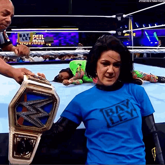 a woman wearing a blue shirt that says bay ley holds a wrestling belt