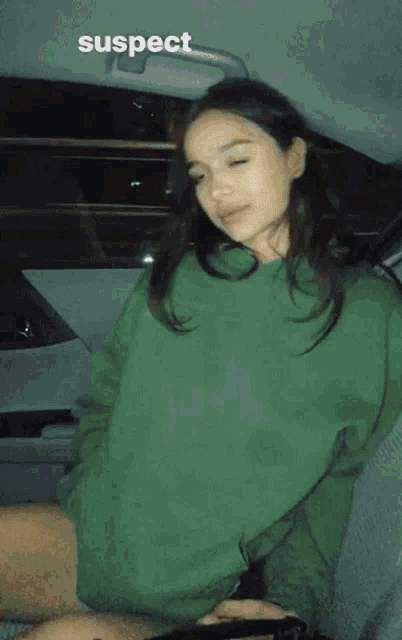 a woman in a green sweatshirt is sitting in the back seat of a car with the word suspect above her head
