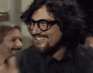 a man with glasses and a beard is smiling in a crowd .