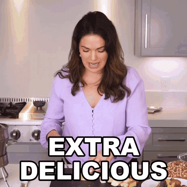 a woman in a purple shirt is standing in a kitchen with the words extra delicious written above her