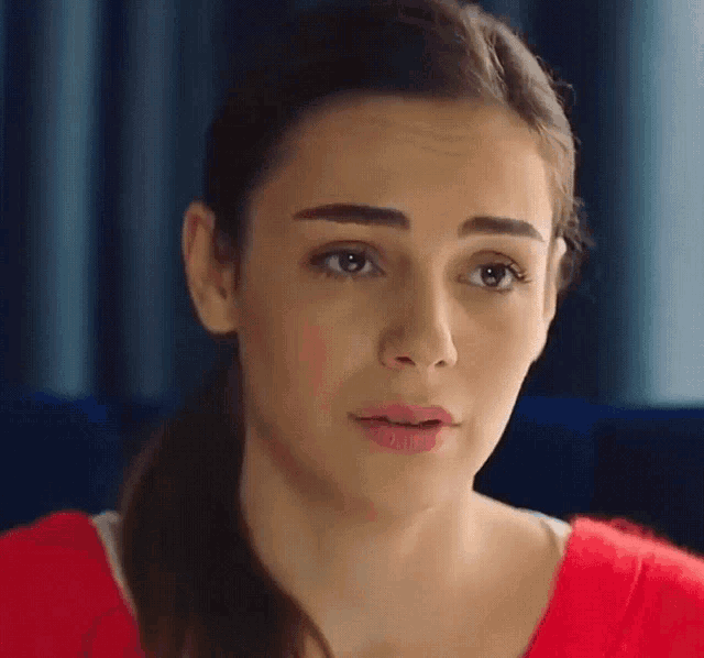 a woman in a red shirt is looking at the camera with a ponytail .