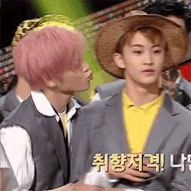 a man with pink hair is kissing another man with a straw hat .