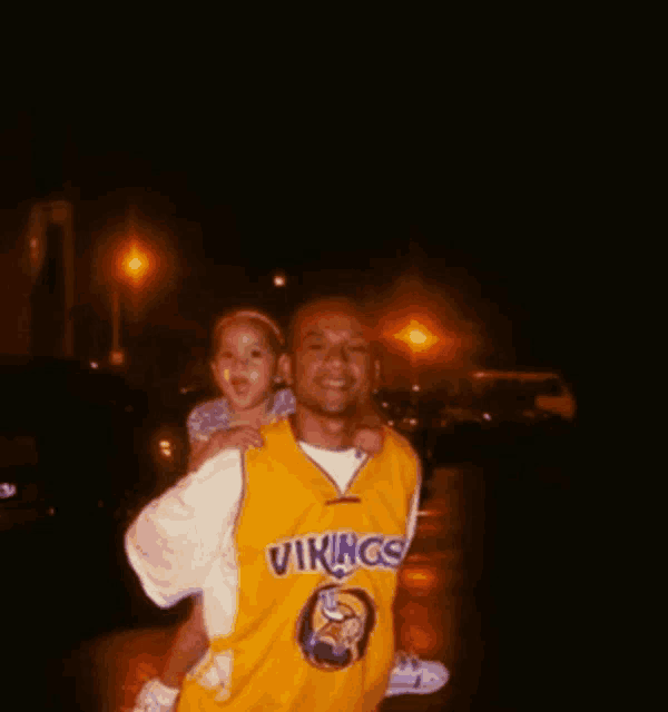 a man wearing a vikings jersey holds a little girl